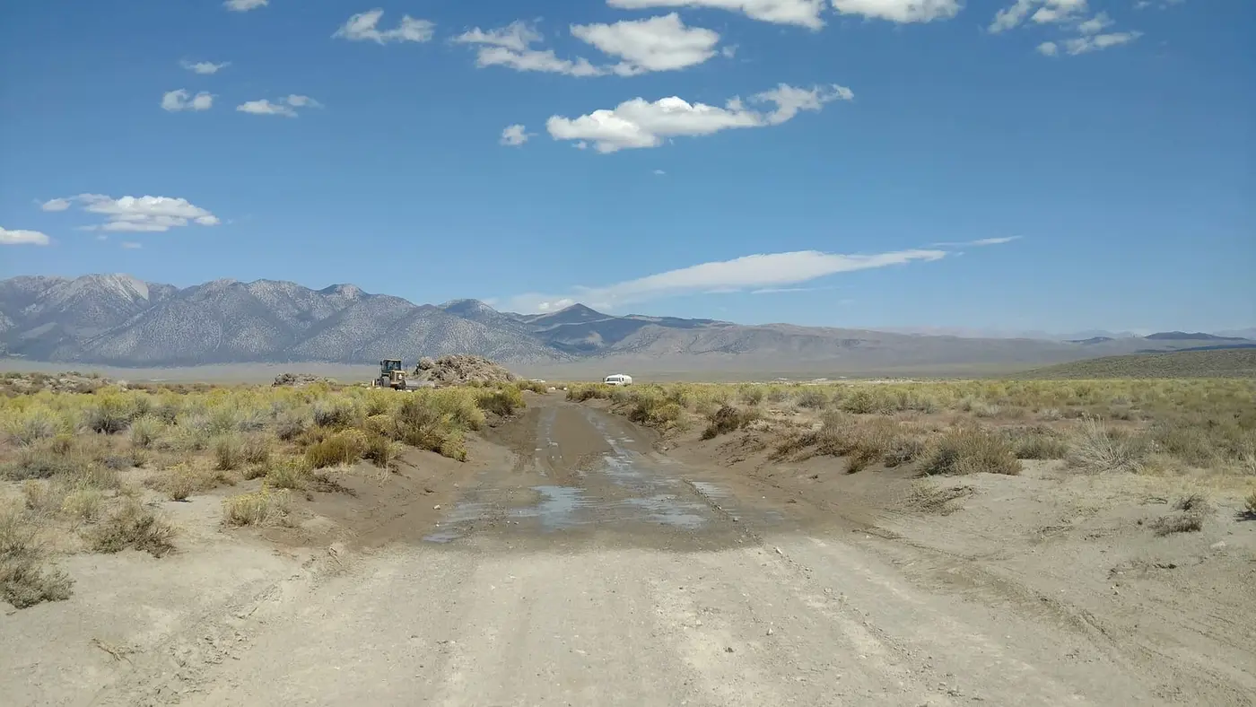 Dirt access road to Wild Willy's Hot Spring crossing sagebrush in Long Valley toward distant mountains