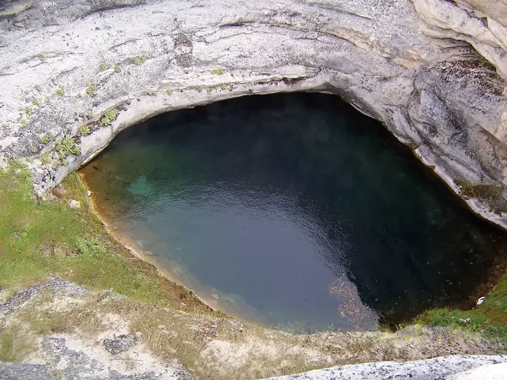 Dark green spring water at the bottom of Diana's Punch Bowl, a sheer walled travertine crater