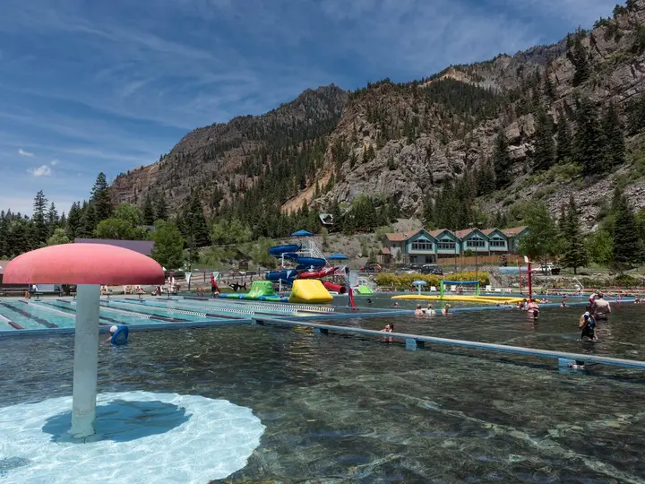 Large outdoor hot springs pool with a mushroom fountain below the red cliffs of Ouray
