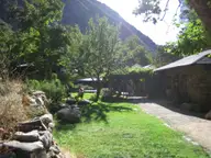 Stone buildings and a green lawn at Tassajara beneath a steep forested canyon wall