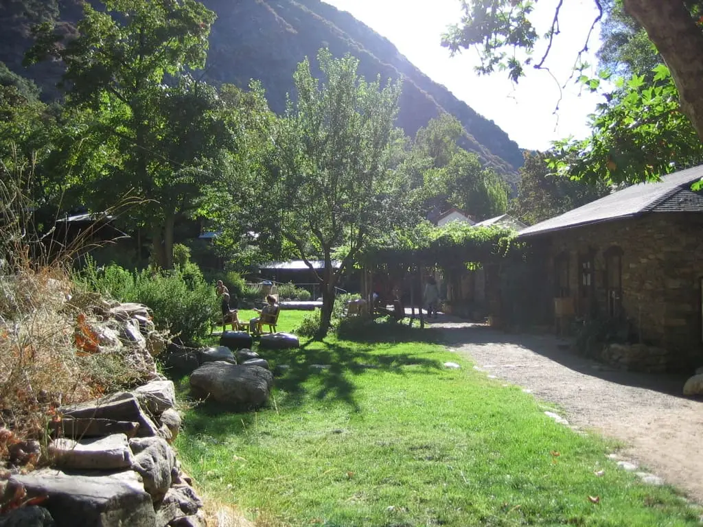 Stone buildings and a green lawn at Tassajara beneath a steep forested canyon wall