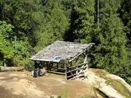 Weathered wooden shelter over the Umpqua Hot Springs soaking pool on a travertine ledge in conifer forest