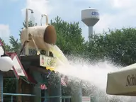 Giant tipping bucket pouring water into a pool at Cserkeszőlő bath, with the water tower behind