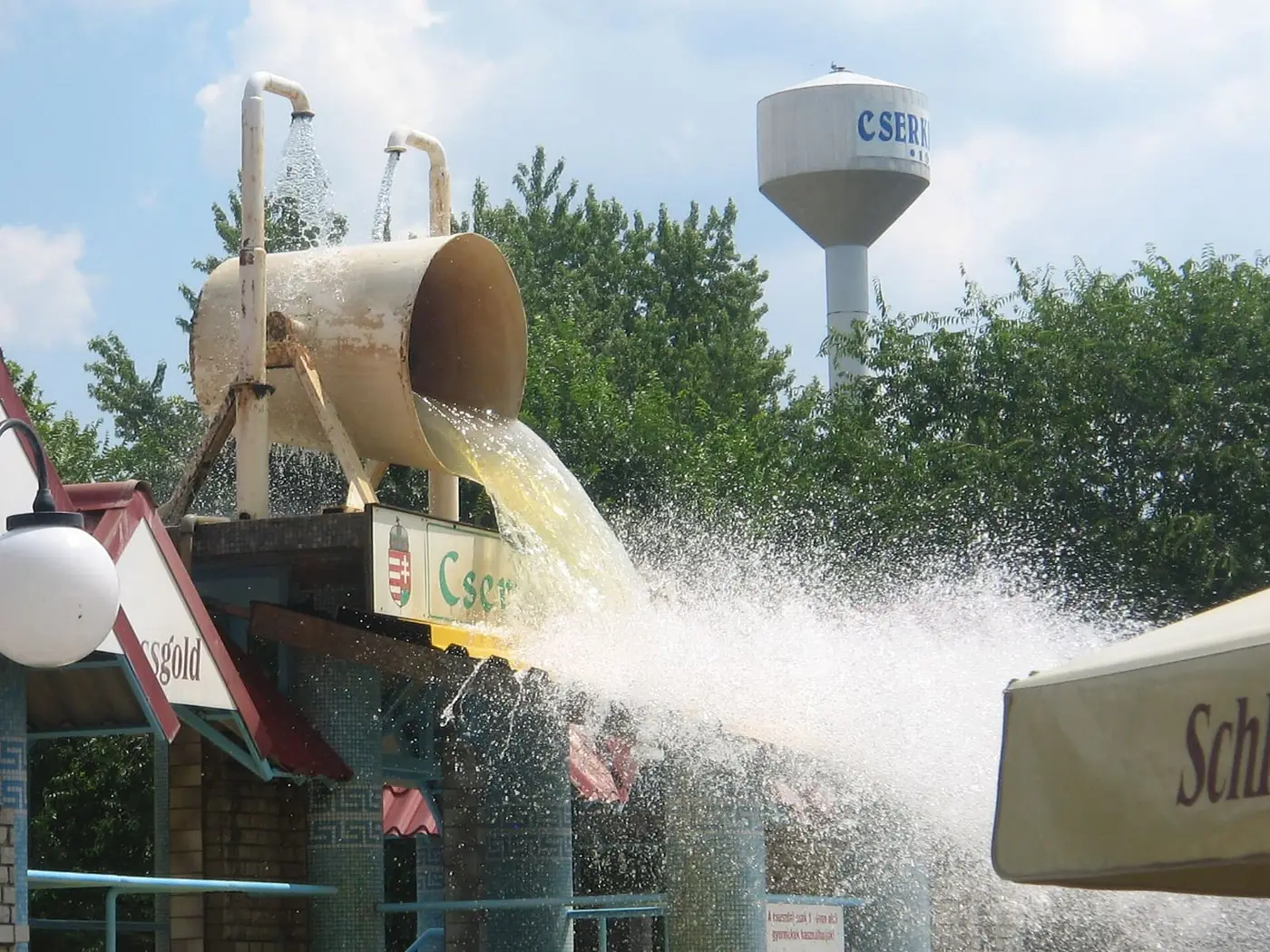 Giant tipping bucket pouring water into a pool at Cserkeszőlő bath, with the water tower behind