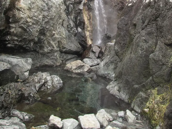 Steaming hot waterfall pouring between rocks into a clear pool at Hot Springs Cove
