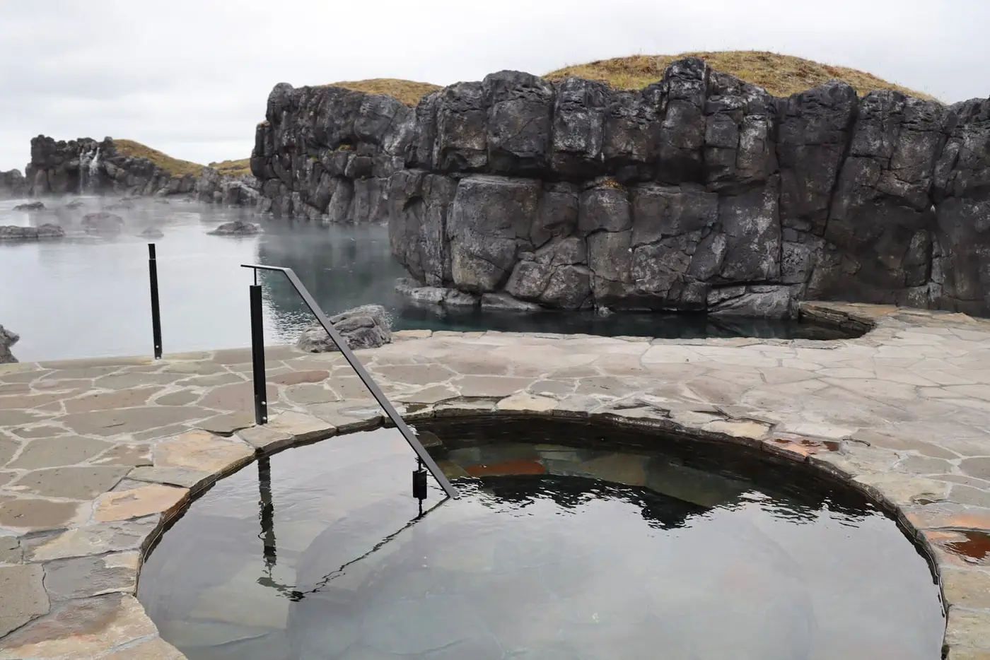Round cold plunge pool on stone paving beside the Sky Lagoon and its rocky cliff wall