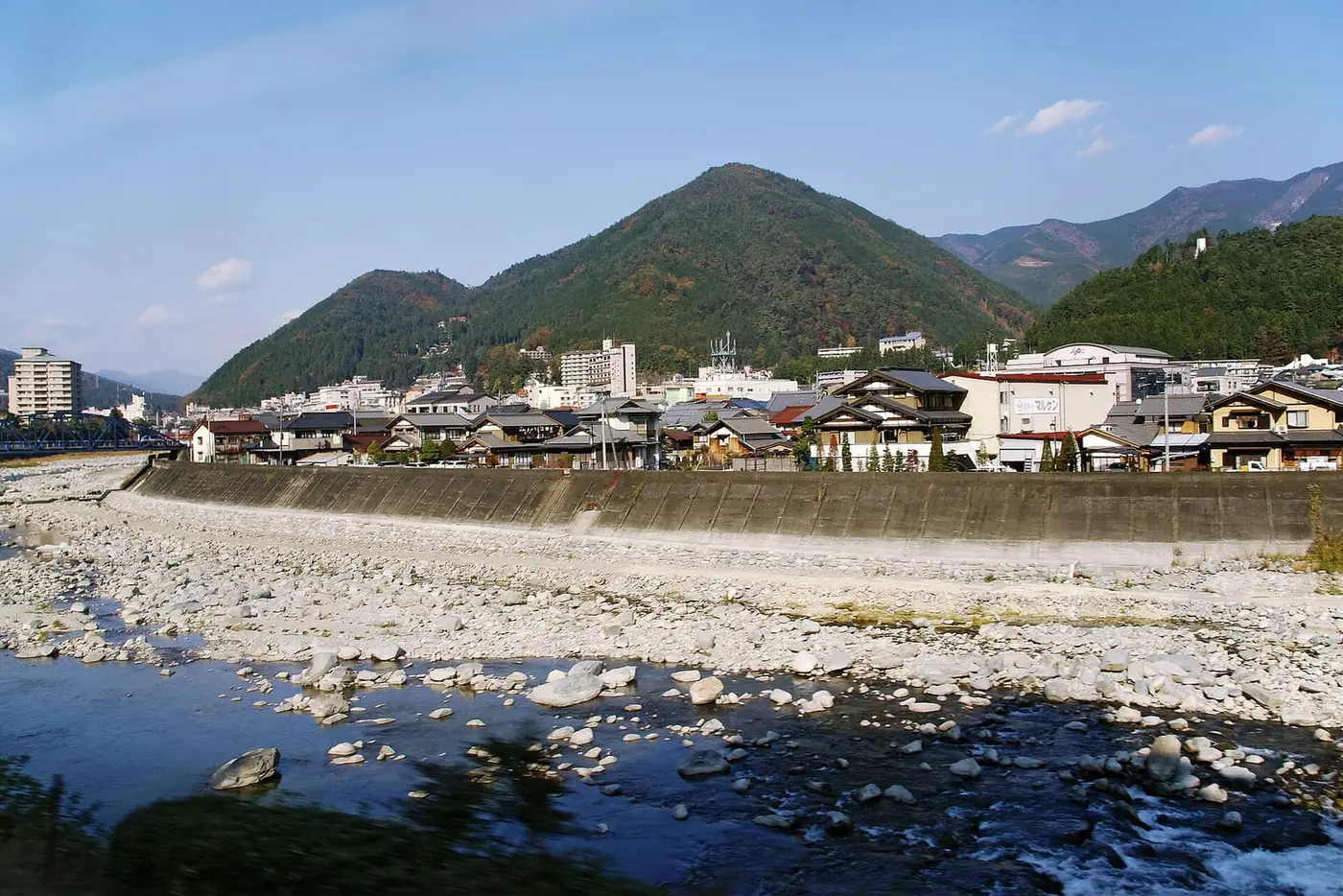 Gero Onsen hotels lining the rocky Hida River below green mountains on a clear day