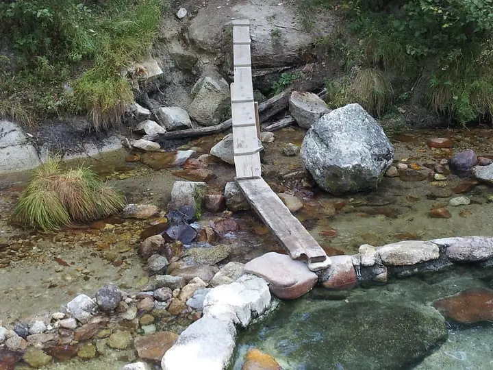 Rock and mortar soaking pool beside Trail Creek with a plank footbridge over the stones