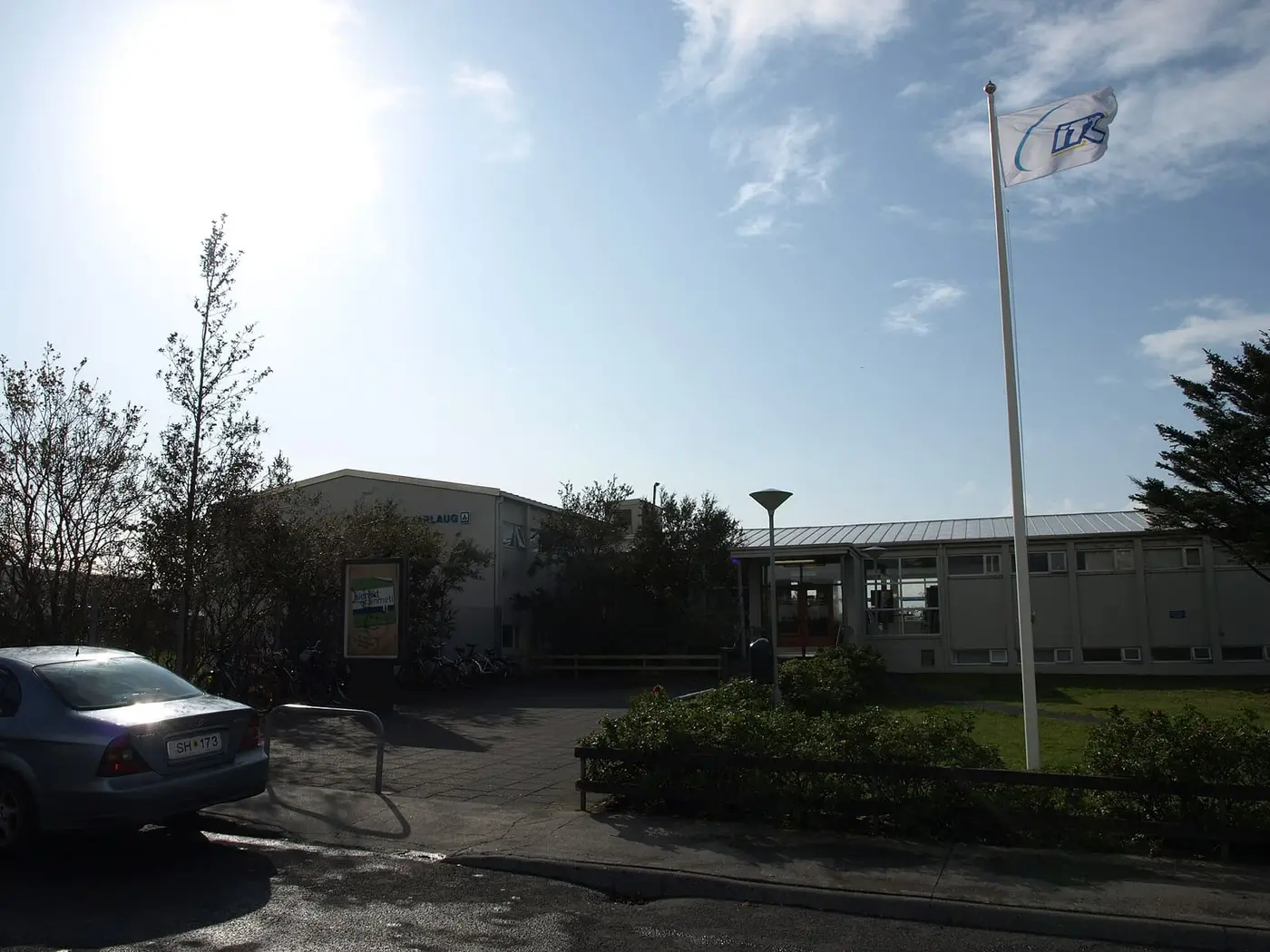 Entrance to the Vesturbæjarlaug pool building with a flagpole, shrubs and trees in west Reykjavík