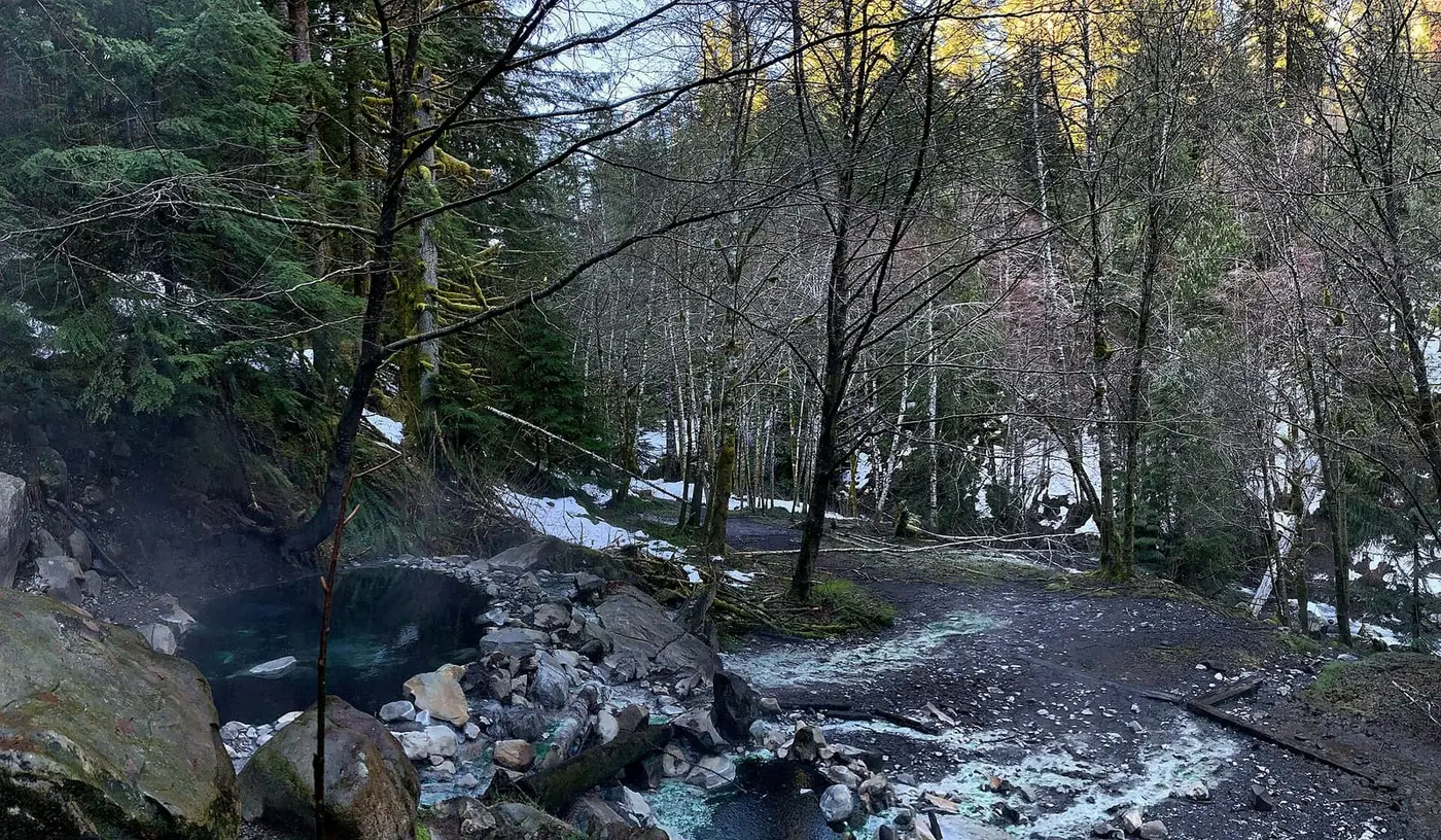 Steaming rock and mud pool beside Boulder Creek at Olympic Hot Springs in a snowy winter forest