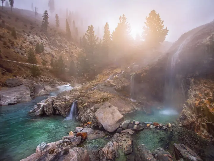 Hot waterfalls spilling over rocks into turquoise pools at Kirkham Hot Springs in soft morning light