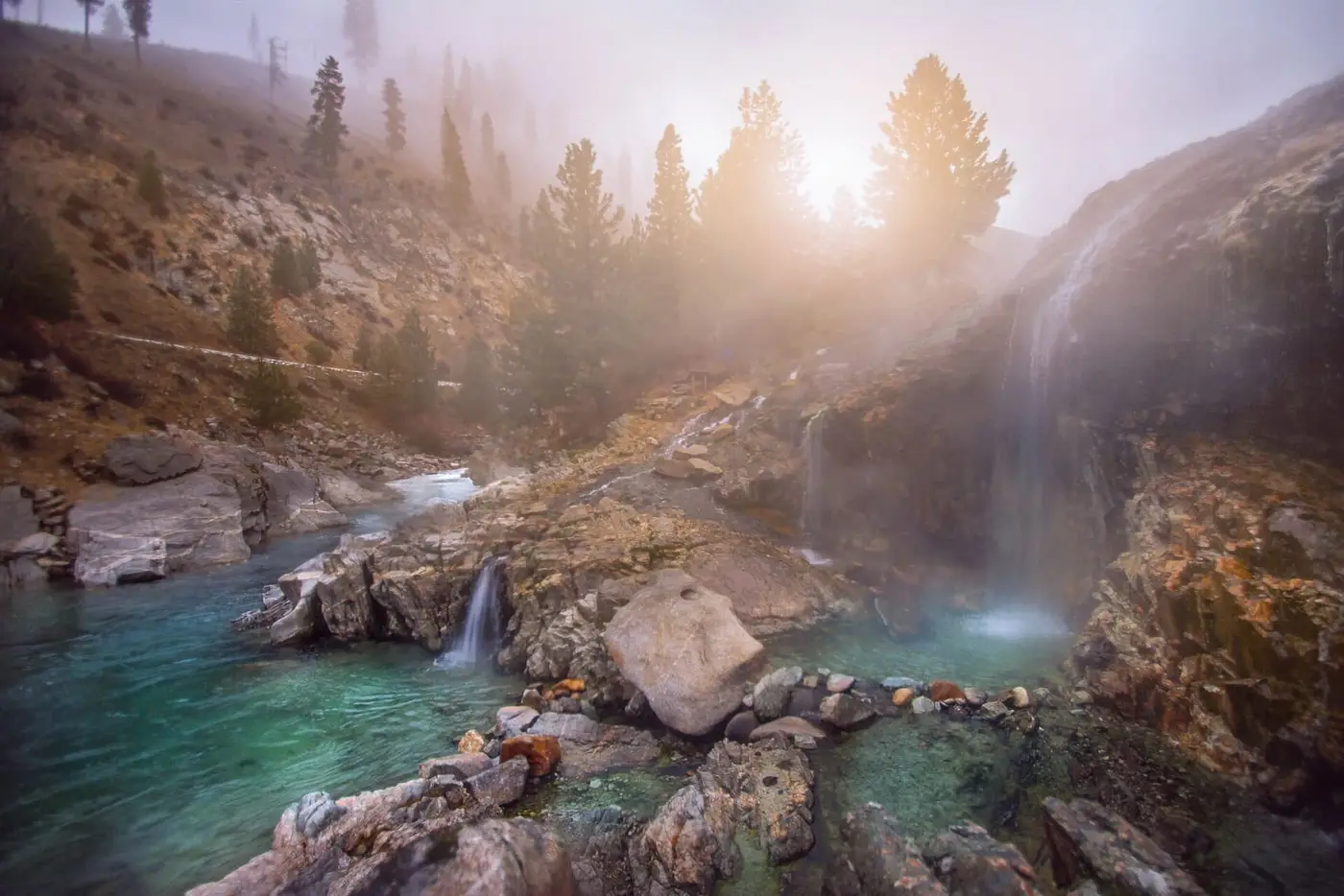 Hot waterfalls spilling over rocks into turquoise pools at Kirkham Hot Springs in soft morning light