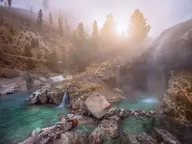 Hot waterfalls spilling over rocks into turquoise pools at Kirkham Hot Springs in soft morning light