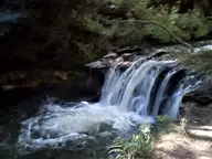 Warm geothermal waterfall pouring into a dark bathing pool at Kerosene Creek