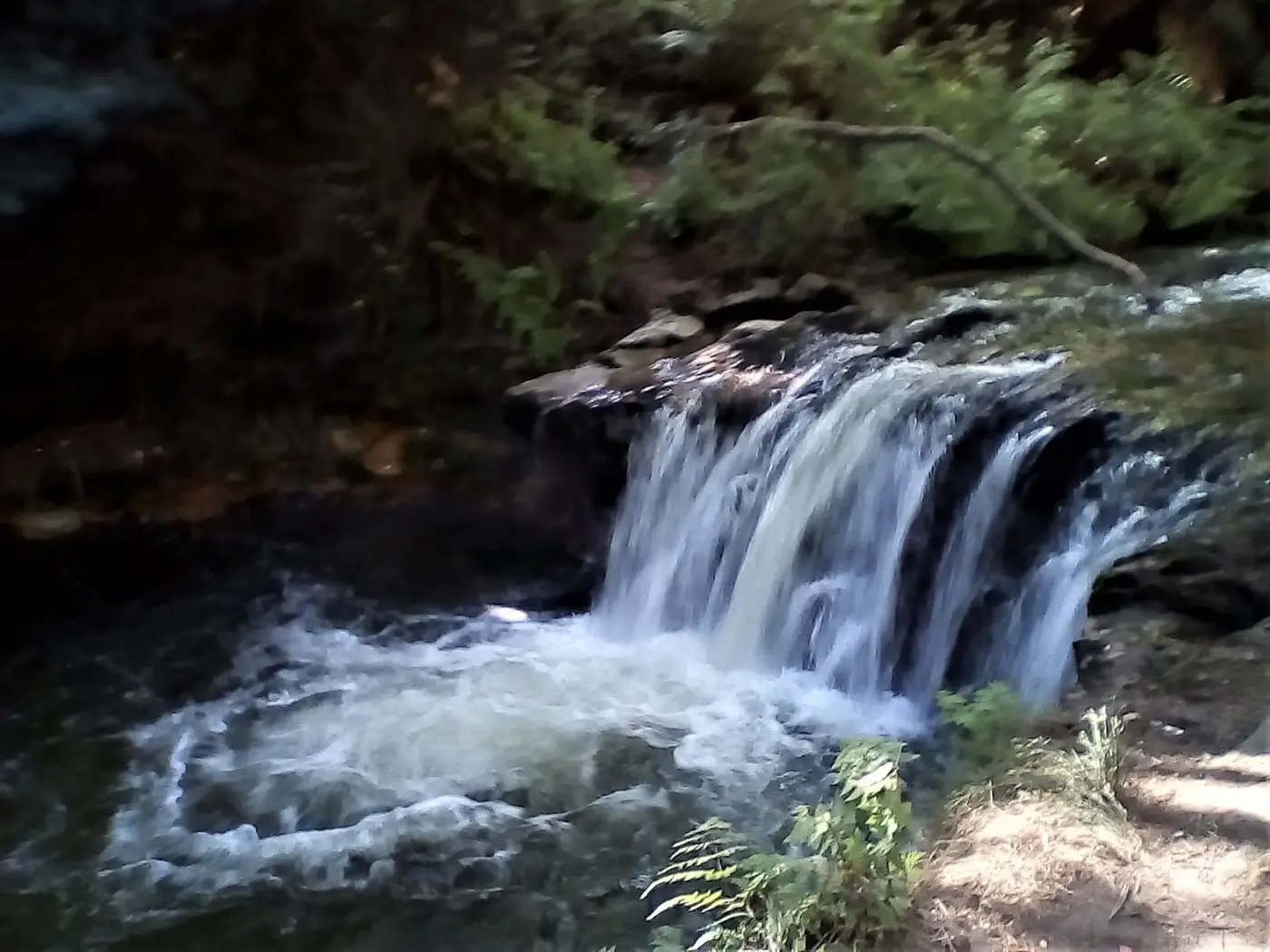 Warm geothermal waterfall pouring into a dark bathing pool at Kerosene Creek