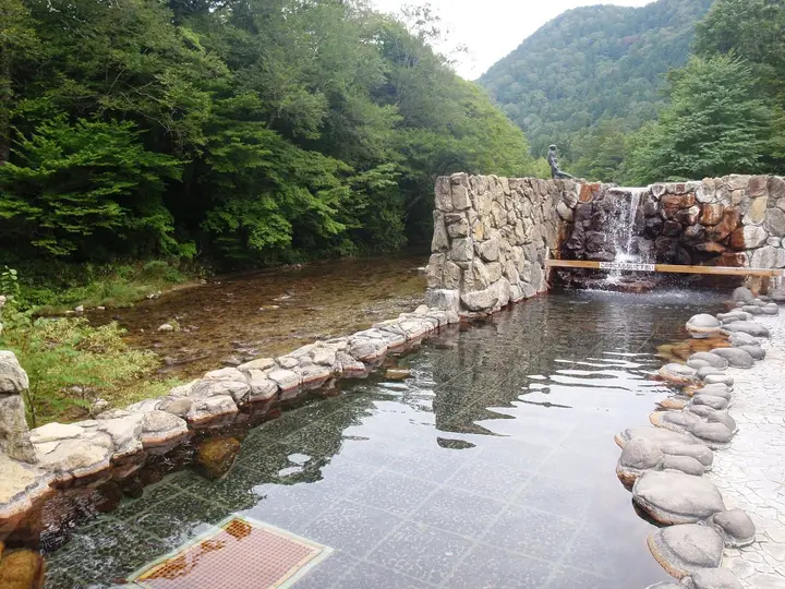 Stone lined open air pool of Meoto Kappa no Yu at Okuyagen beside a forested river