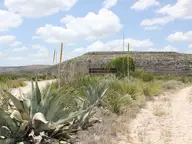 Agave plants beside a dirt road and entrance sign below a flat topped mesa at Devils River State Natural Area