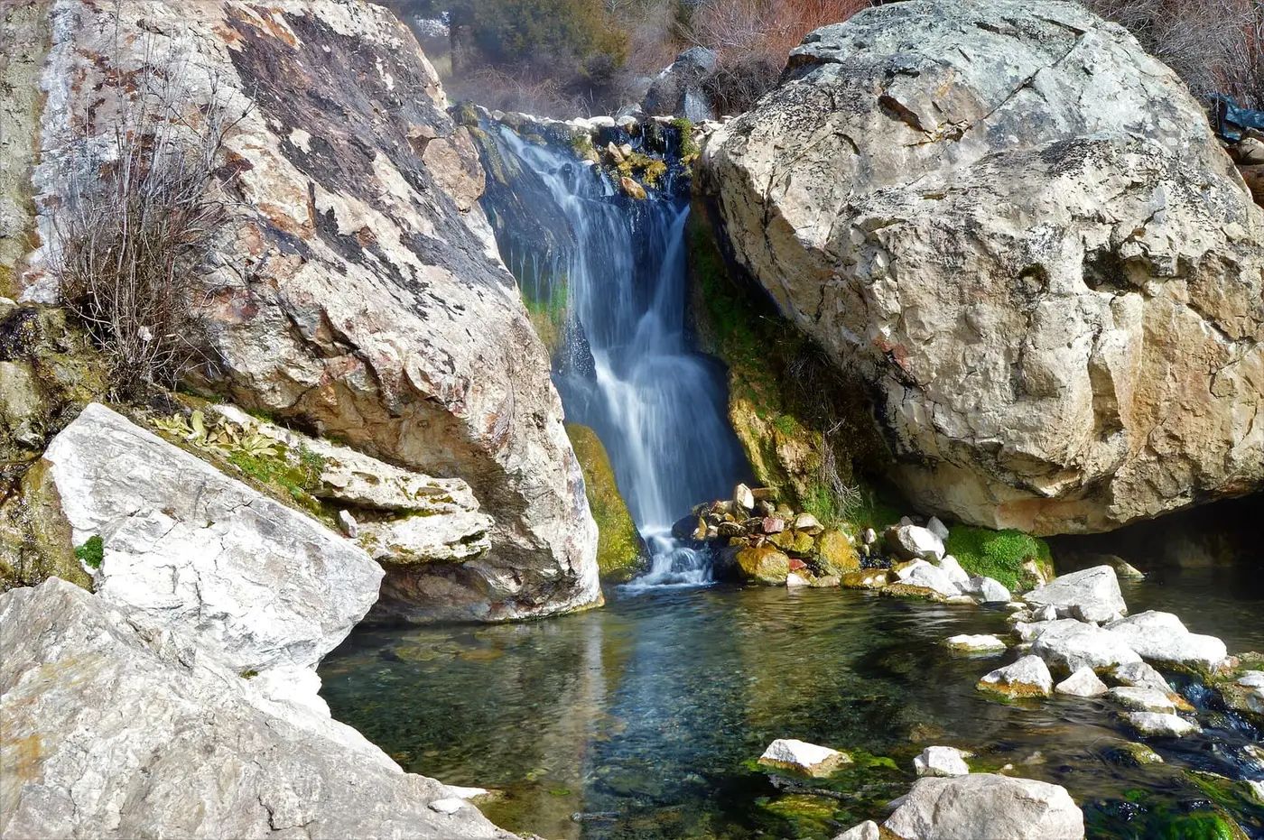 Waterfall pouring between large boulders into a clear rock-lined pool at Goldbug Hot Springs