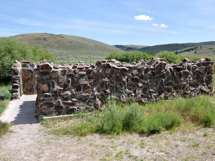 Stone walls enclosing the Hart Mountain Hot Springs bathing pool beside a gravel path and rolling hills