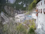 Old stone buildings of the Bagni Vecchi in Bormio perched on a cliff, with an outdoor pool