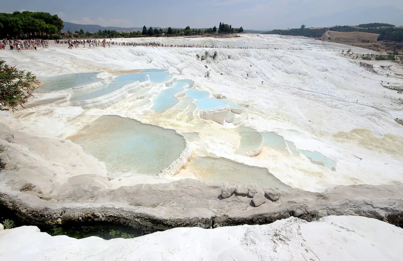 Pale blue thermal pools on the white travertine terraces of Pamukkale under a hazy sky