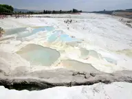 Pale blue thermal pools on the white travertine terraces of Pamukkale under a hazy sky