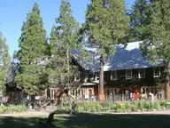 Main lodge at Breitenbush Hot Springs behind tall conifers and a sunny front lawn