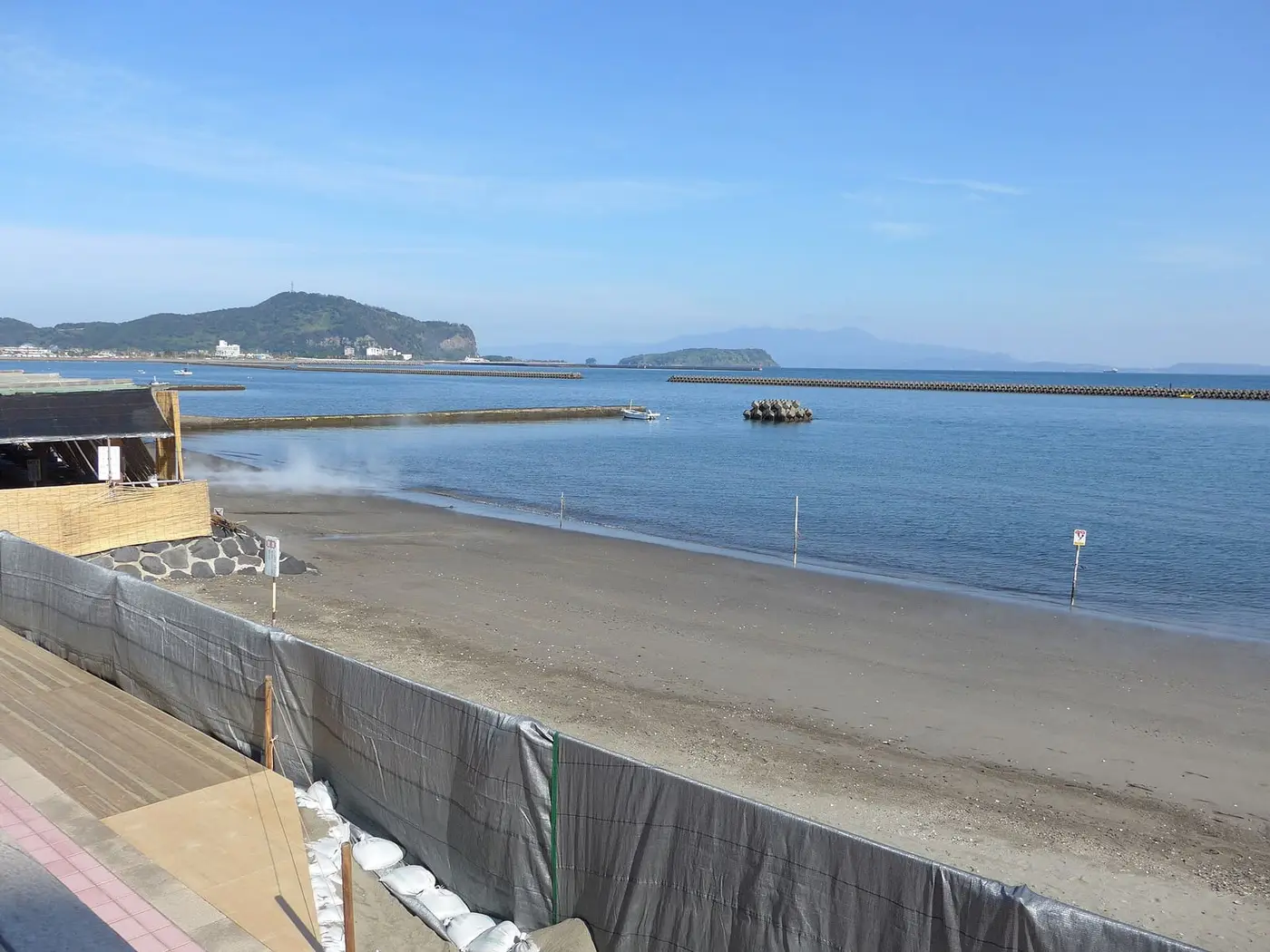 Steam rising from the sand bath beach at Ibusuki beside calm Kagoshima Bay and a small island