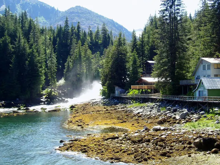 Houses on a boardwalk beside a rushing waterfall and rocky tidal shore at Baranof Warm Springs