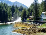 Houses on a boardwalk beside a rushing waterfall and rocky tidal shore at Baranof Warm Springs