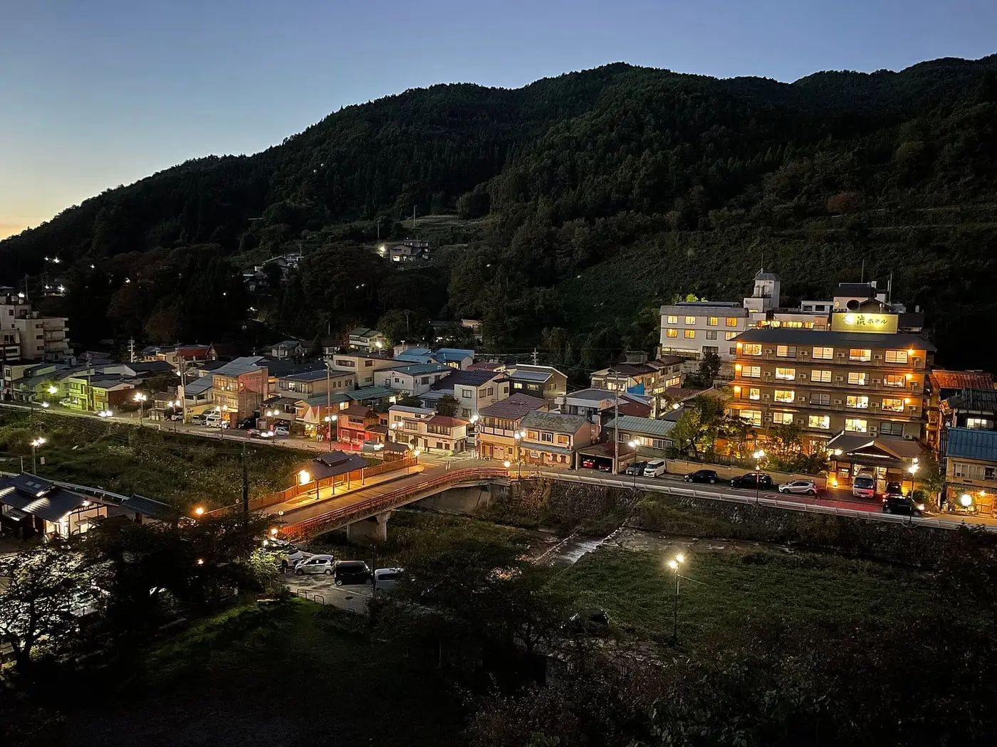Shibu Onsen village at dusk with lit inns and a bridge below forested mountains