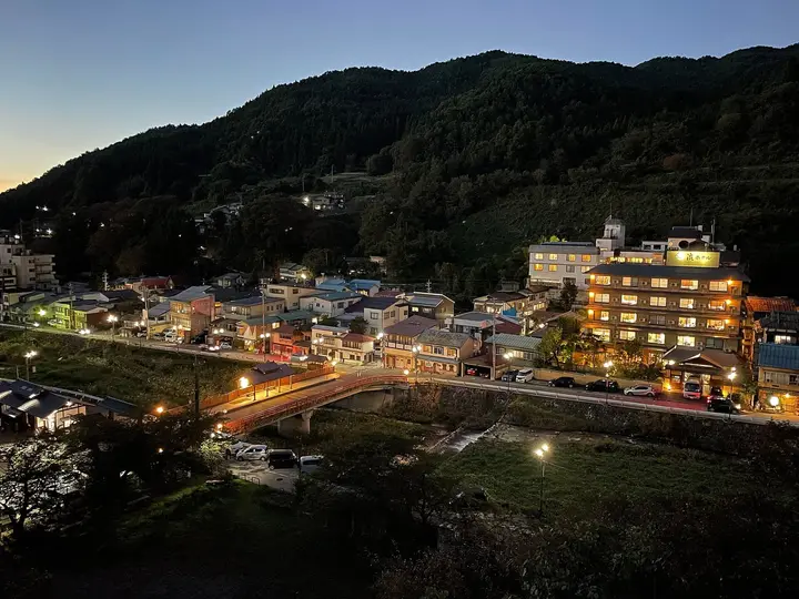 Shibu Onsen village at dusk with lit inns and a bridge below forested mountains