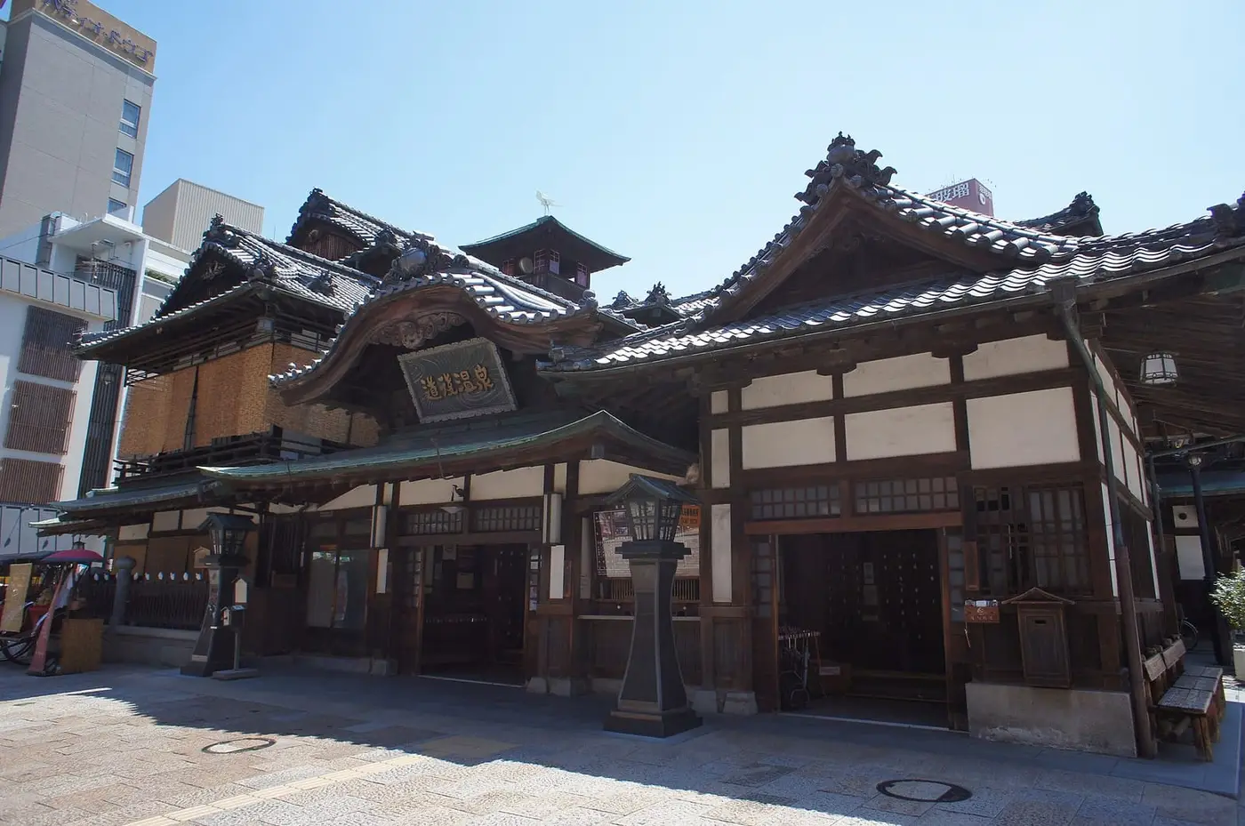 Wooden multi roofed facade of Dogo Onsen Honkan bathhouse under a clear blue sky