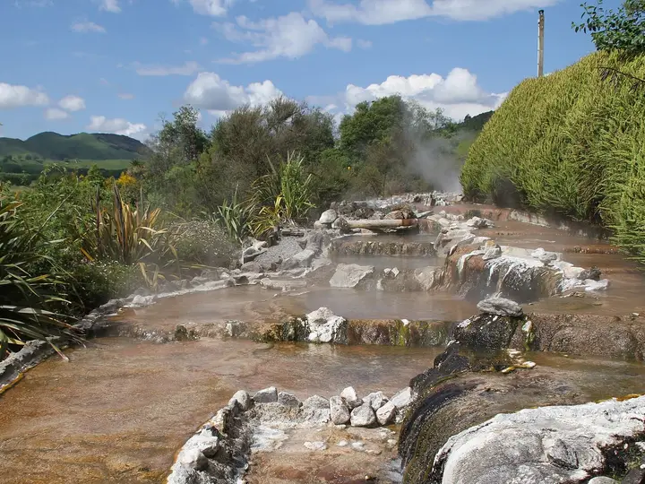 Steaming hot stream flowing over pale sinter terraces in Waikite Valley under a blue sky