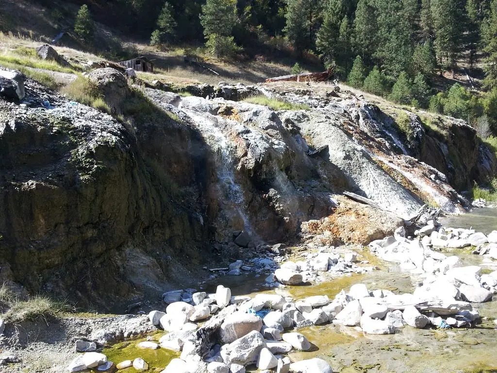 Hot water spilling over mineral crusted rock terraces at Bonneville Hot Springs below pine forest