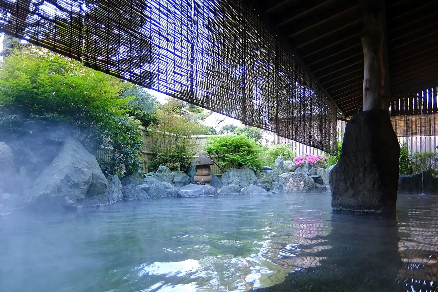 Steaming rock lined open air bath under a bamboo blind at a Tamatsukuri Onsen inn
