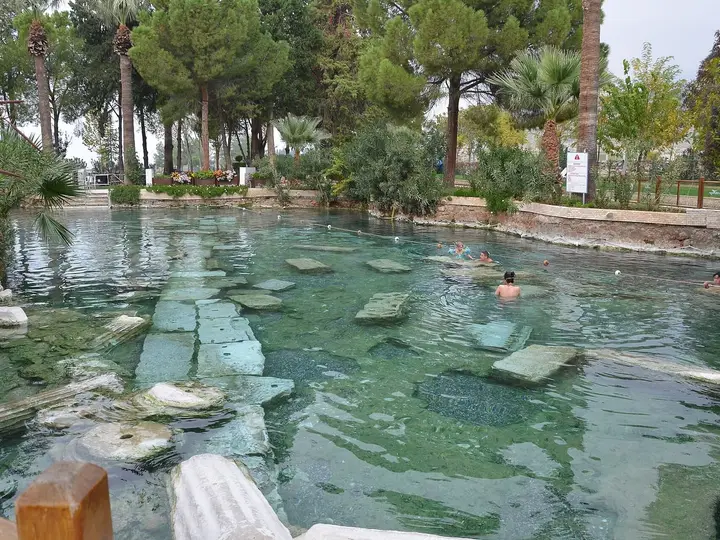 Clear green water of Cleopatra's Pool at Hierapolis with sunken marble columns and pine trees
