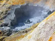 Gray bubbling mudpot ringed by yellow and orange mineral deposits at Sulphur Works in Lassen Volcanic National Park