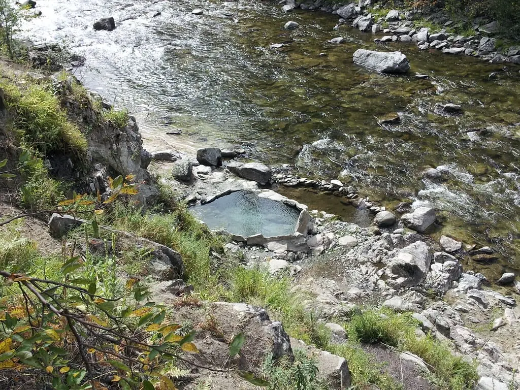 Small rock-lined hot spring pool at Mile 16 Hot Springs on the bank of a clear rocky river