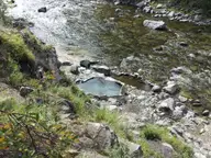 Small rock-lined hot spring pool at Mile 16 Hot Springs on the bank of a clear rocky river