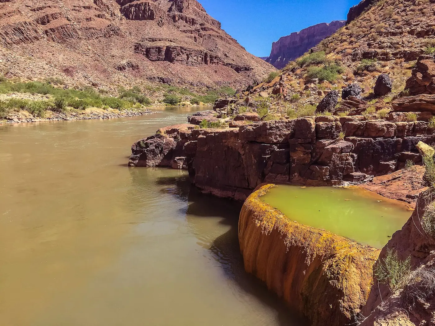Orange travertine bowl of green water at Pumpkin Spring beside the Colorado River in Grand Canyon