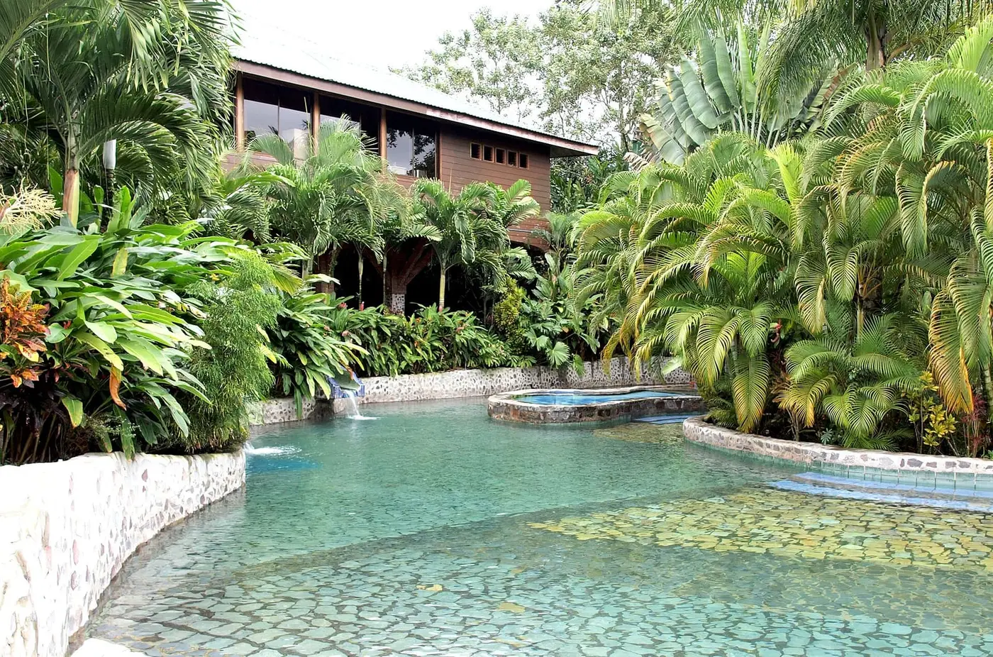 Clear turquoise thermal pool with tiled ledges among tropical plants at Baldi Hot Springs