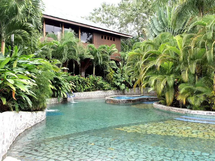 Clear turquoise thermal pool with tiled ledges among tropical plants at Baldi Hot Springs
