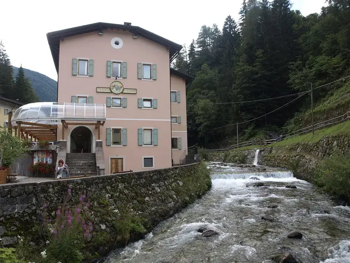 Pink Terme di Rabbi spa building with green shutters beside a rushing mountain stream
