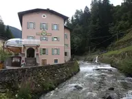 Pink Terme di Rabbi spa building with green shutters beside a rushing mountain stream