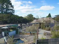 Wooden fenced pool enclosures and walkways of the Ngawha Springs complex under a blue sky