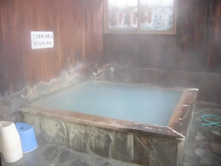 Steaming milky hot spring tub with stone edges in a wooden bathroom at Sukayu Onsen