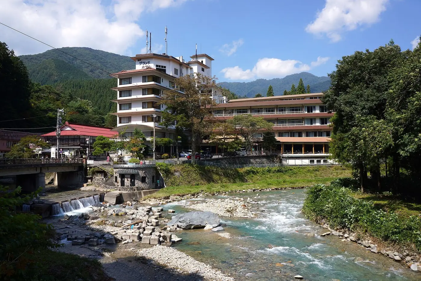 Clear river running over rocks past hotels in the Shima Onsen valley under blue sky