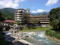 Clear river running over rocks past hotels in the Shima Onsen valley under blue sky