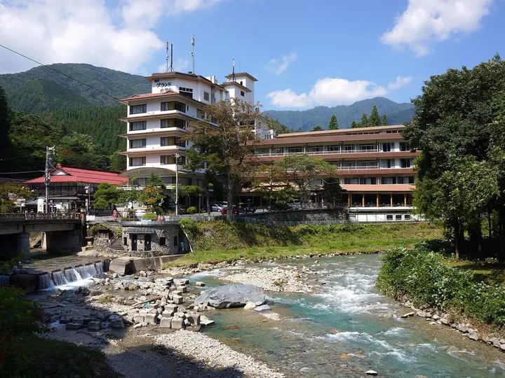 Clear river running over rocks past hotels in the Shima Onsen valley under blue sky